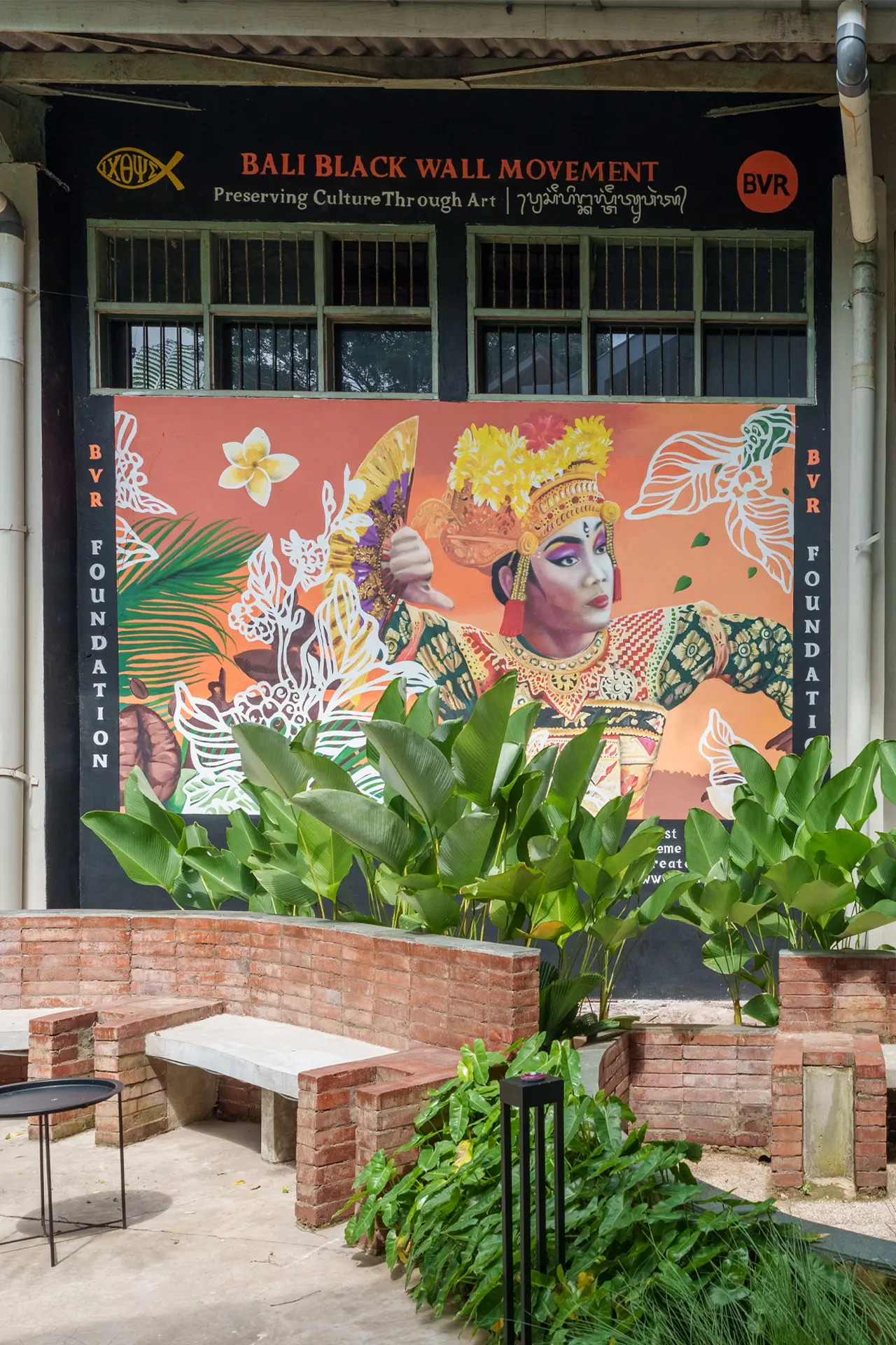 A BVR Foundation cultural-preservation art display framed by plants in a courtyard.
